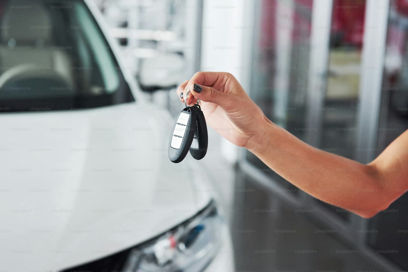 Hand holding car keys beside a white vehicle in a dealership showroom